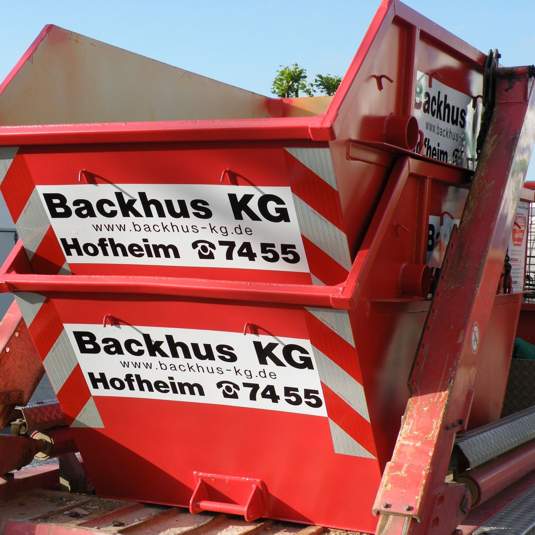 Zwei ineinander gestapelte Container mit der Aufschrift Backhus KG sind auf einen LKW geladen.
