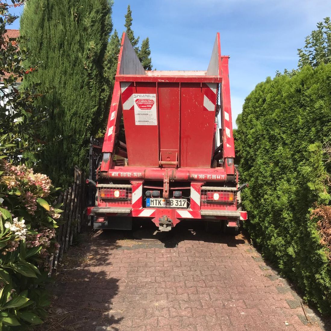 LKW, beladen mit rotem Container der Firma Backhus, fährt durch eine enge Gasse.