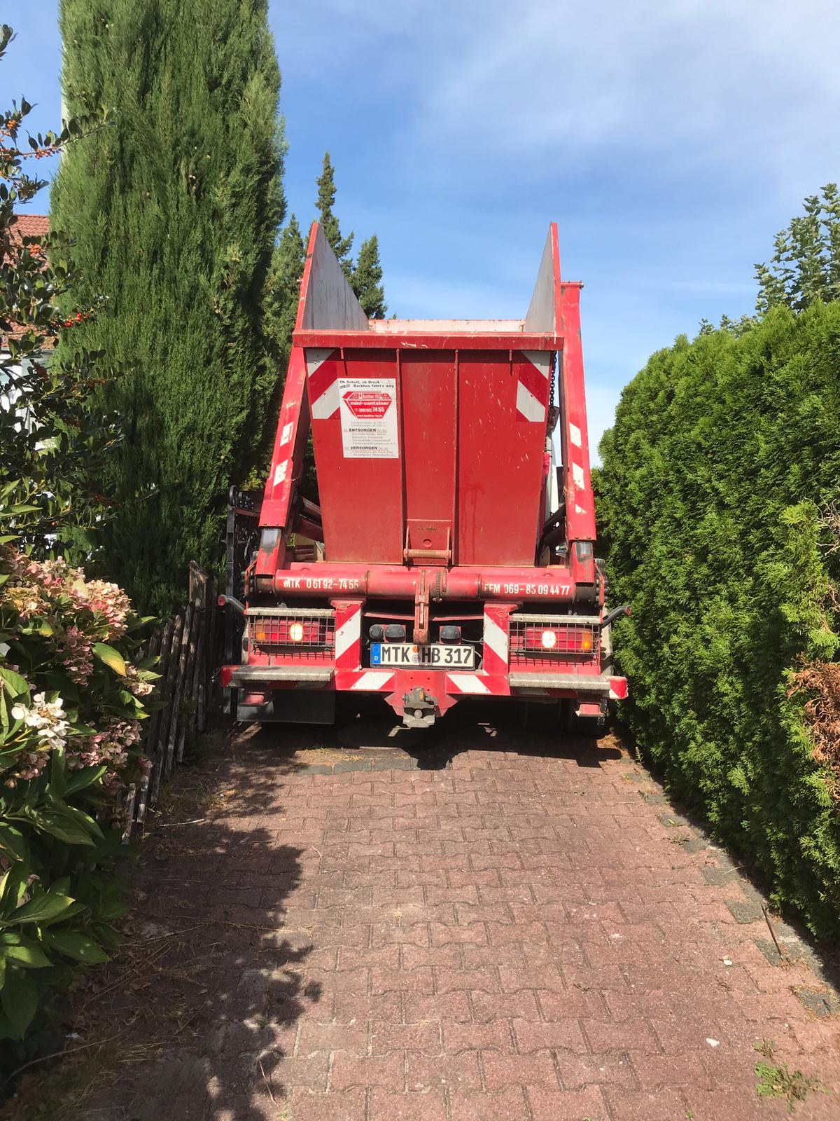 LKW, beladen mit rotem Container der Firma Backhus, fährt durch eine enge Gasse.