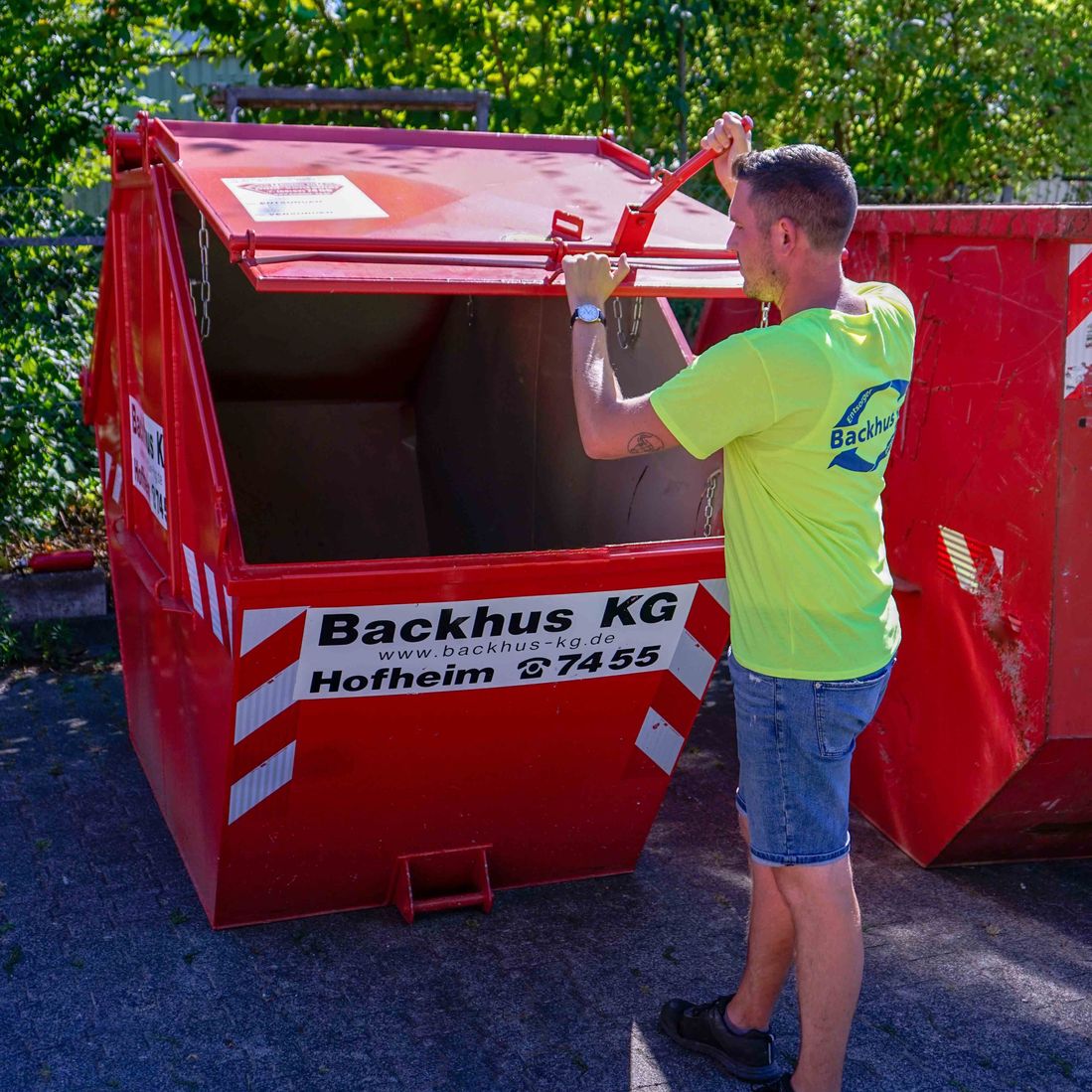 Mann öffnet roten kleinen Container der Firma Backhus KG.