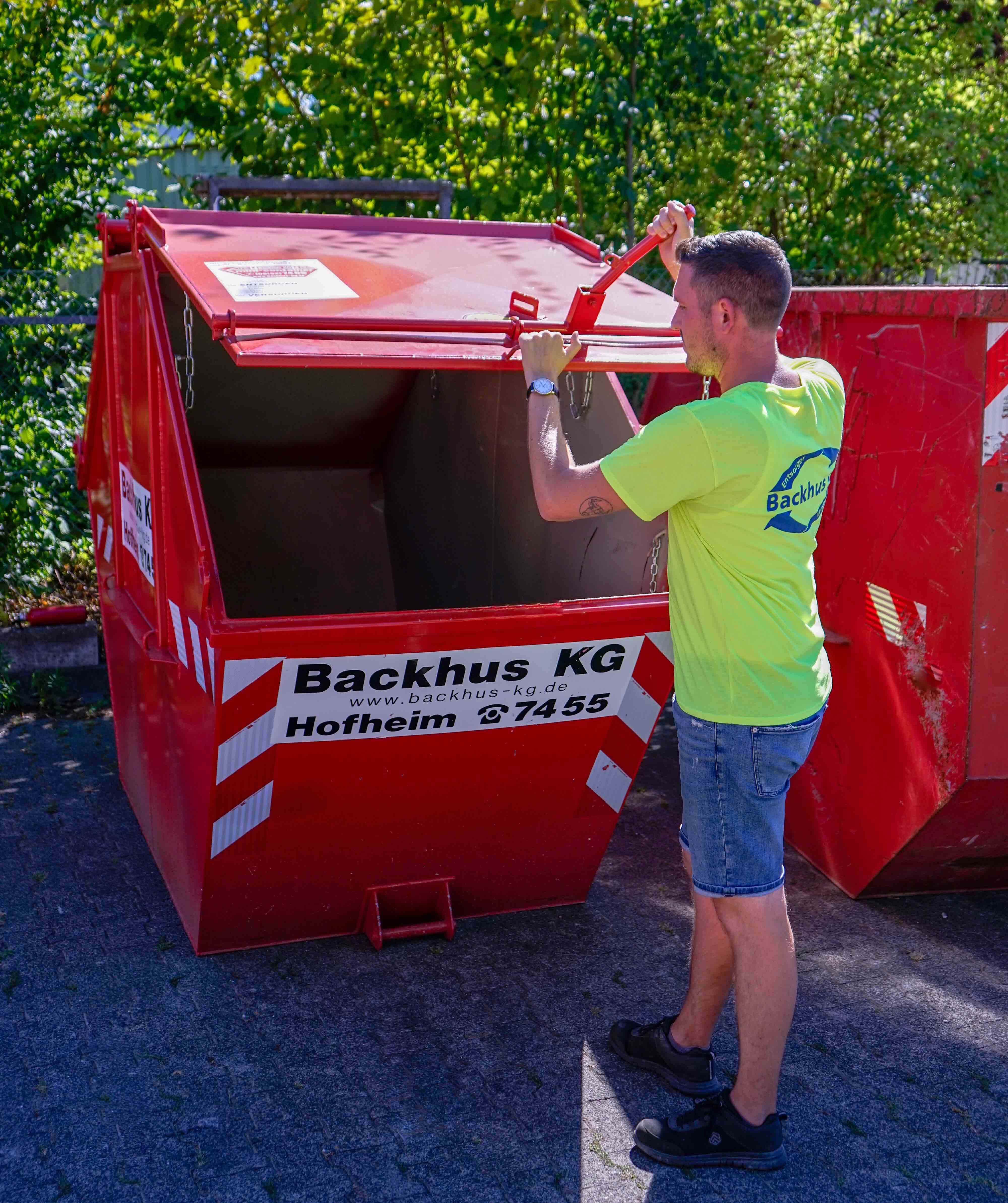 Mann öffnet roten kleinen Container der Firma Backhus KG.